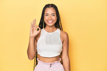 Foto de Joven mujer indonesia en amarillo estudio telón de fondo alegre y confiado mostrando gesto ok. - Imagen libre de derechos