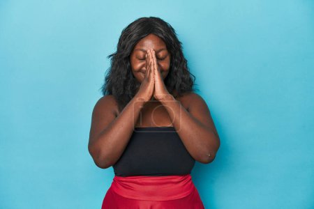 Téléchargez les photos : Jeune femme courbée afro-américaine tenant la main dans la prière près de la bouche, se sent confiant. - en image libre de droit
