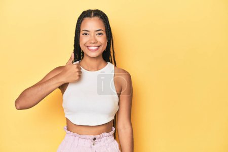 Photo for Young Indonesian woman on yellow studio backdrop smiling and raising thumb up - Royalty Free Image
