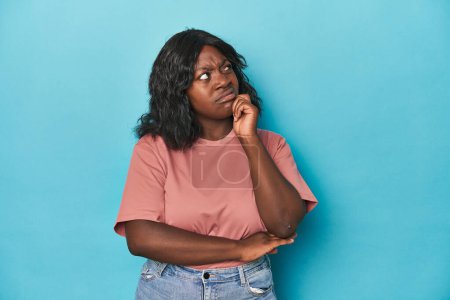 Photo for Young african american curvy woman thinking and looking up, being reflective, contemplating, having a fantasy. - Royalty Free Image