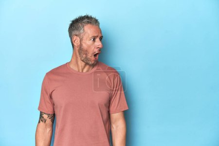 Photo for Middle-aged caucasian man on blue backdrop being shocked because of something she has seen. - Royalty Free Image