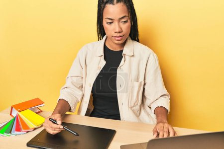 Téléchargez les photos : Designer indonésien avec tablette graphique, PC et palette de couleurs sur studio jaune - en image libre de droit