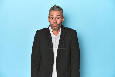 Photo for Caucasian businessman, middle-aged on blue background shrugs shoulders and open eyes confused. - Royalty Free Image