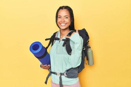 Foto de Mujer indonesia listo para el viaje de montaña en amarillo que muestra un gesto de llamada de teléfono móvil con los dedos. - Imagen libre de derechos
