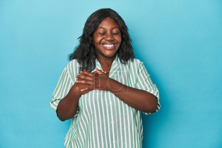 Foto de Joven africana americana curvilínea riendo manteniendo las manos en el corazón, concepto de felicidad. - Imagen libre de derechos