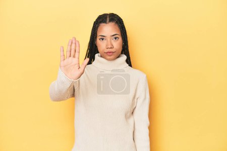 Téléchargez les photos : Jeune femme indonésienne sur fond de studio jaune debout avec la main tendue montrant le panneau stop, vous empêchant. - en image libre de droit