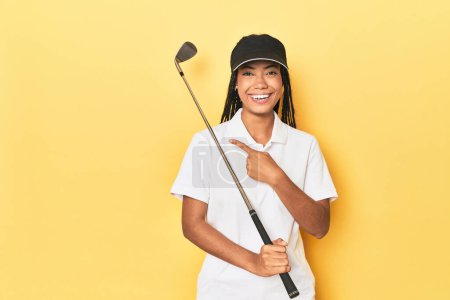 Photo for Indonesian female golfer on yellow backdrop smiling and pointing aside, showing something at blank space. - Royalty Free Image