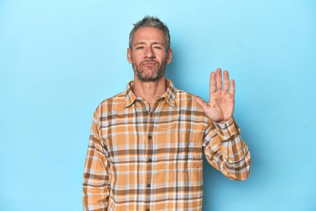 Foto de Hombre caucásico de mediana edad sobre fondo azul sonriente alegre mostrando el número cinco con los dedos. - Imagen libre de derechos