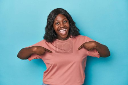 Foto de Joven africana americana curvilínea mujer sorprendida señalando con el dedo, sonriendo ampliamente. - Imagen libre de derechos