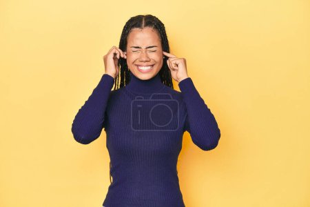 Téléchargez les photos : Jeune femme indonésienne sur fond de studio jaune couvrant les oreilles avec les mains. - en image libre de droit