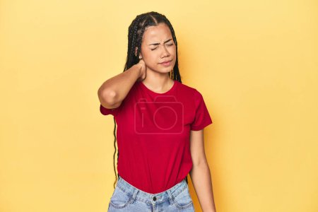Photo for Young Indonesian woman on yellow studio backdrop having a neck pain due to stress, massaging and touching it with hand. - Royalty Free Image