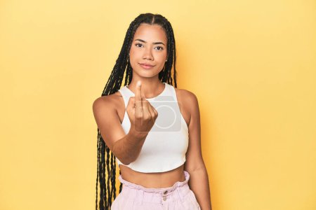 Foto de Joven mujer indonesia en el fondo del estudio amarillo señalándote con el dedo como si invitaras a acercarte. - Imagen libre de derechos