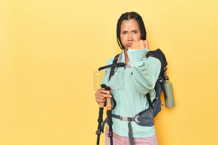 Téléchargez les photos : Femme indonésienne avec équipement de randonnée sur jaune montrant poing à caméra, expression faciale agressive. - en image libre de droit