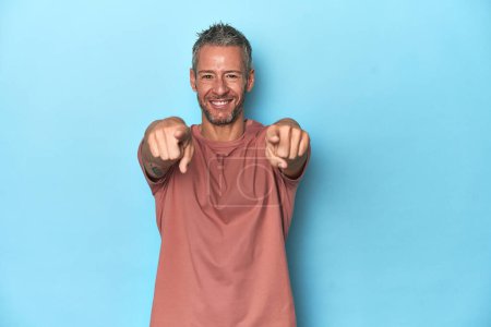 Photo for Middle-aged caucasian man on blue backdrop cheerful smiles pointing to front. - Royalty Free Image