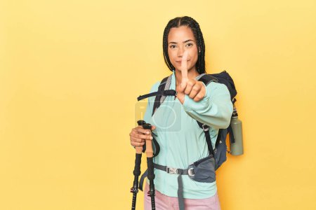 Foto de Mujer indonesia con equipo de senderismo en amarillo mostrando el número uno con el dedo. - Imagen libre de derechos