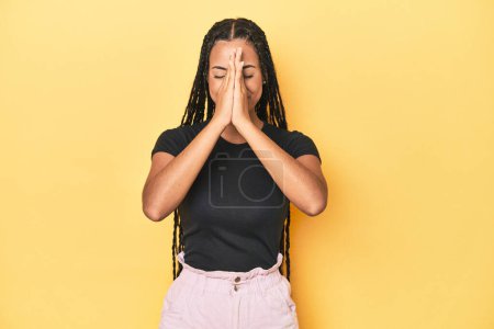 Photo for Young Indonesian woman on yellow studio backdrop holding hands in pray near mouth, feels confident. - Royalty Free Image