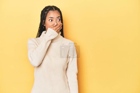 Photo for Young Indonesian woman on yellow studio backdrop thoughtful looking to a copy space covering mouth with hand. - Royalty Free Image