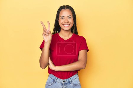 Téléchargez les photos : Jeune Indonésienne sur fond de studio jaune montrant numéro deux avec les doigts. - en image libre de droit