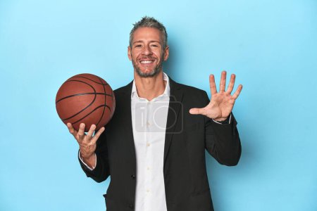Photo for Middle-aged basketball coach on blue backdrop Middle-aged basketball coach on blue backdropsmiling cheerful showing number five with fingers. - Royalty Free Image