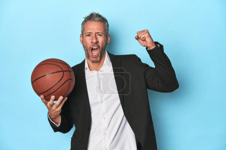 Photo for Middle-aged basketball coach on blue backdrop Middle-aged basketball coach on blue backdropraising fist after a victory, winner concept. - Royalty Free Image