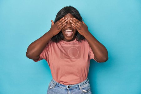 Téléchargez les photos : Jeune femme courbée afro-américaine couvre les yeux avec les mains, sourit largement en attendant une surprise. - en image libre de droit