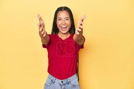 Téléchargez les photos : Jeune femme indonésienne sur fond de studio jaune se sent confiant donnant un câlin à la caméra. - en image libre de droit