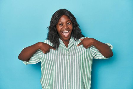 Foto de Joven africana americana curvilínea mujer sorprendida señalando con el dedo, sonriendo ampliamente. - Imagen libre de derechos