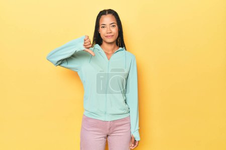Photo for Indonesian sporty woman on yellow backdrop showing a dislike gesture, thumbs down. Disagreement concept. - Royalty Free Image