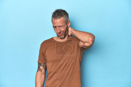 Photo for Middle-aged caucasian man on blue backdrop suffering neck pain due to sedentary lifestyle. - Royalty Free Image