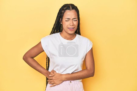 Photo for Young Indonesian woman on yellow studio backdrop having a liver pain, stomach ache. - Royalty Free Image