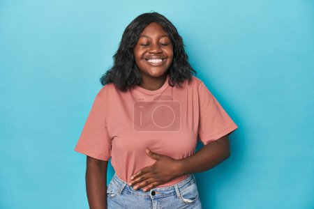 Téléchargez les photos : Jeune femme afro-américaine courbée touche le ventre, sourit doucement, manger et concept de satisfaction. - en image libre de droit