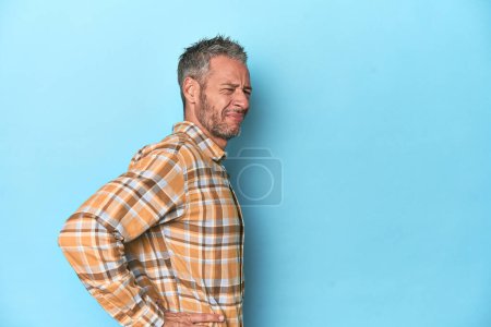 Photo for Middle-aged caucasian man on blue backdrop suffering a back pain. - Royalty Free Image