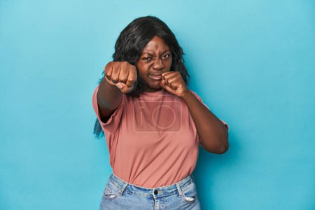 Foto de Joven mujer con curvas afroamericana lanzando un puñetazo, ira, lucha debido a una discusión, boxeo. - Imagen libre de derechos