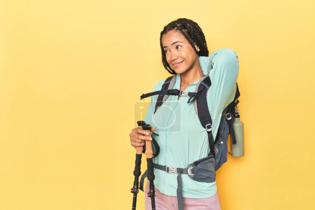 Photo for Indonesian woman with hiking gear on yellow touching back of head, thinking and making a choice. - Royalty Free Image