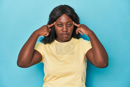 Photo for Young african american curvy woman focused on a task, keeping forefingers pointing head. - Royalty Free Image