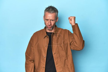 Photo for Middle-aged caucasian man on blue backdrop showing fist to camera, aggressive facial expression. - Royalty Free Image