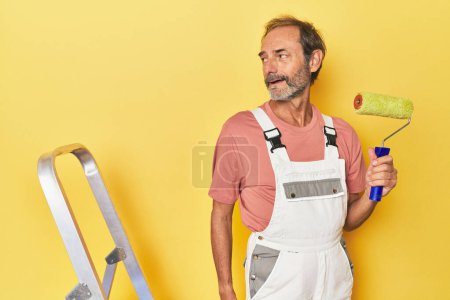 Foto de Hombre pintura amarillo telón de fondo en el estudio se ve a un lado sonriente, alegre y agradable. - Imagen libre de derechos