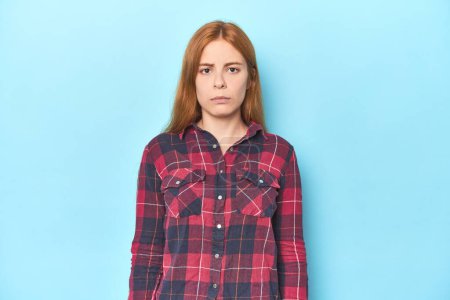 Photo for Redhead young woman on blue background sad, serious face, feeling miserable and displeased. - Royalty Free Image