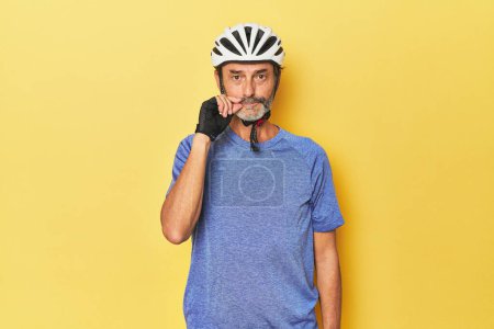 Foto de Ciclista con casco en estudio amarillo con los dedos en los labios manteniendo un secreto. - Imagen libre de derechos