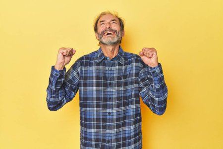 Foto de Hombre caucásico de mediana edad en estudio amarillo celebrando una victoria, pasión y entusiasmo, expresión feliz. - Imagen libre de derechos