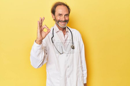 Photo for Doctor with stethoscope in yellow studio cheerful and confident showing ok gesture. - Royalty Free Image