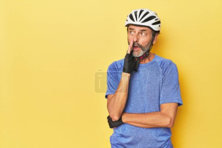Téléchargez les photos : Cycliste portant un casque en studio jaune dit une nouvelle secrète de freinage chaud et regarder de côté - en image libre de droit