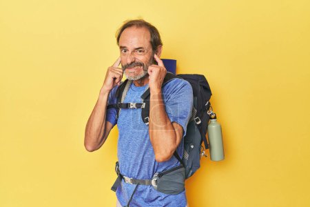 Téléchargez les photos : Randonneur d'âge moyen avec sac à dos en studio couvrant les oreilles avec les mains. - en image libre de droit