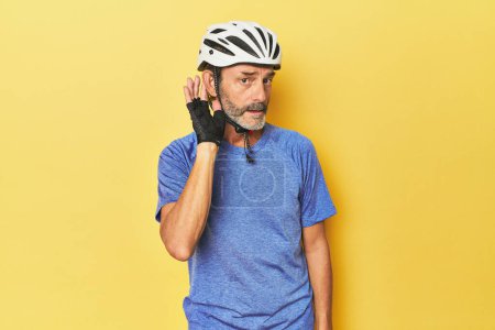Foto de Ciclista con casco en estudio amarillo tratando de escuchar un chisme. - Imagen libre de derechos