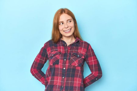 Photo for Redhead young woman on blue background relaxed and happy laughing, neck stretched showing teeth. - Royalty Free Image