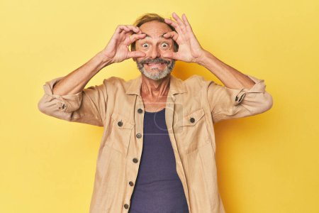 Téléchargez les photos : Homme d'âge moyen caucasien en studio jaune gardant les yeux ouverts pour trouver une opportunité de succès. - en image libre de droit