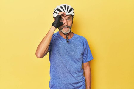 Foto de Ciclista vistiendo casco en estudio amarillo emocionado manteniendo el buen gesto a los ojos. - Imagen libre de derechos