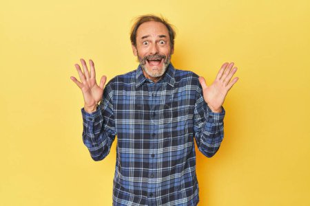 Photo for Caucasian middle-aged man in yellow studio celebrating a victory or success, he is surprised and shocked. - Royalty Free Image