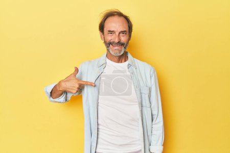 Téléchargez les photos : Homme d'âge moyen caucasien en studio jaune personne pointant à la main vers un espace de copie chemise, fier et confiant - en image libre de droit