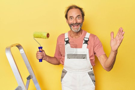 Téléchargez les photos : Homme peignant fond jaune en studio recevant une agréable surprise, excité et levant les mains. - en image libre de droit